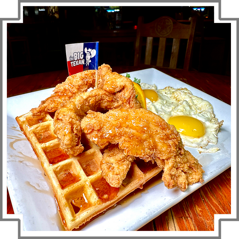 Fried chicken with waffles and eggs on a plate, featuring Big Texan sign in the background.