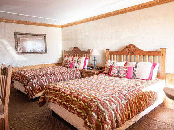 Two wooden beds with patterned bedding in a room with wooden walls and a mirror.
