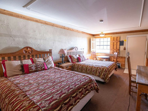 Bedroom with two wooden beds, patterned bedding, and a lamp.