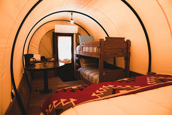 Interior of a compact living space with a full bed, bunk beds, desk, and single door.