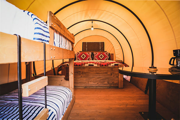 Interior of a compact living space with canvas "tent" style roof with bunk beds, a large bed and a small table.