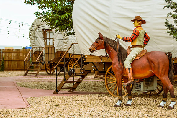 Cowboy Statue on a house next to a covered wagon.
