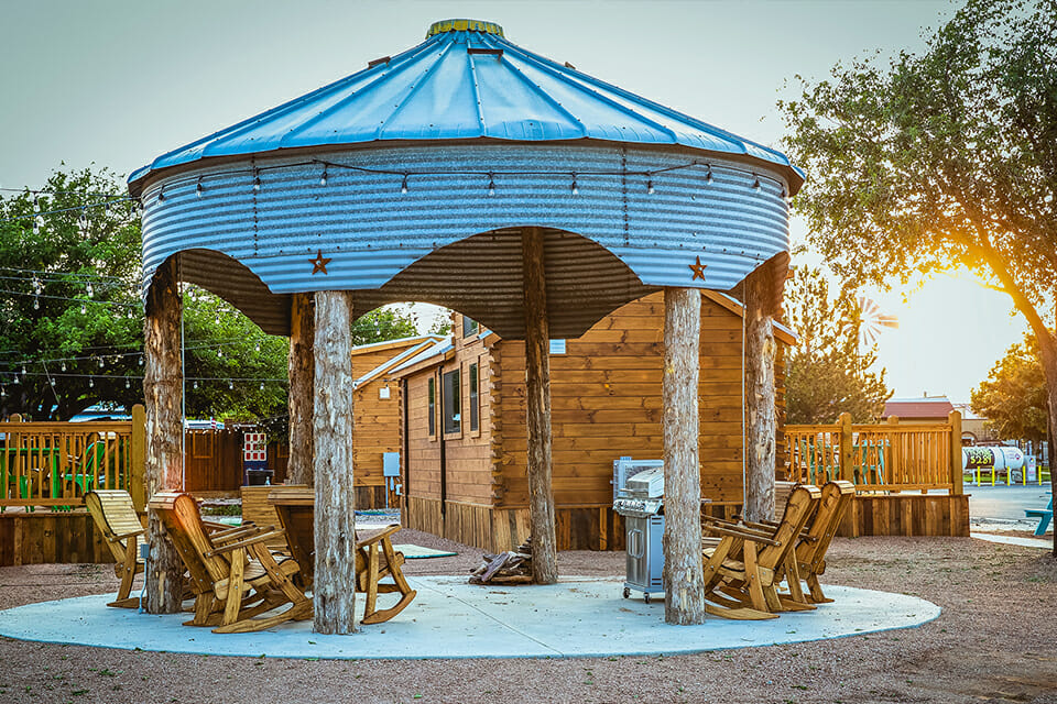 Wooden gazebo with a blue roof in an outdoor setting with chairs and tables.