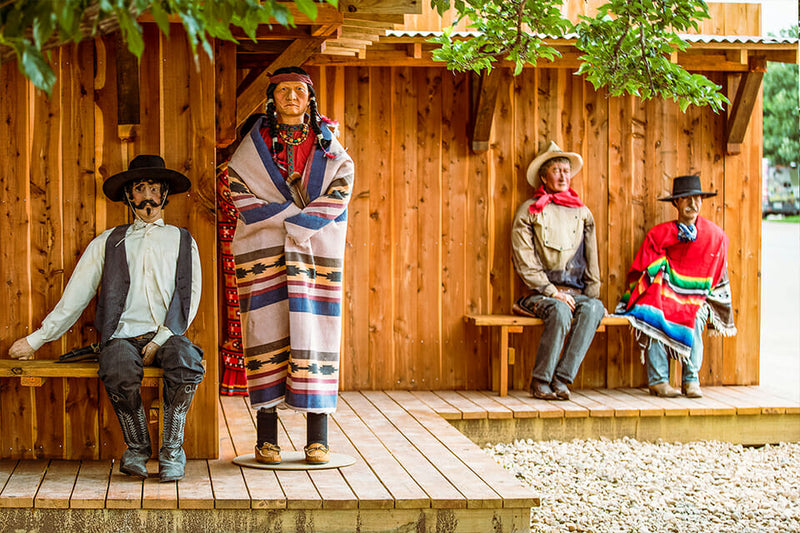 Four mannequins in traditional Native American attire sitting on a wooden platform.