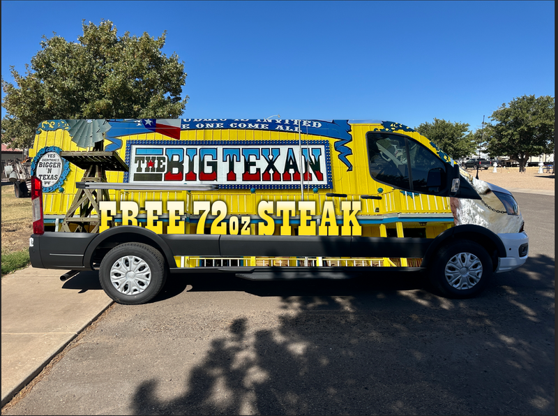 Van decorated with 'The Big Texan' branding and promotional text on a sunny day.