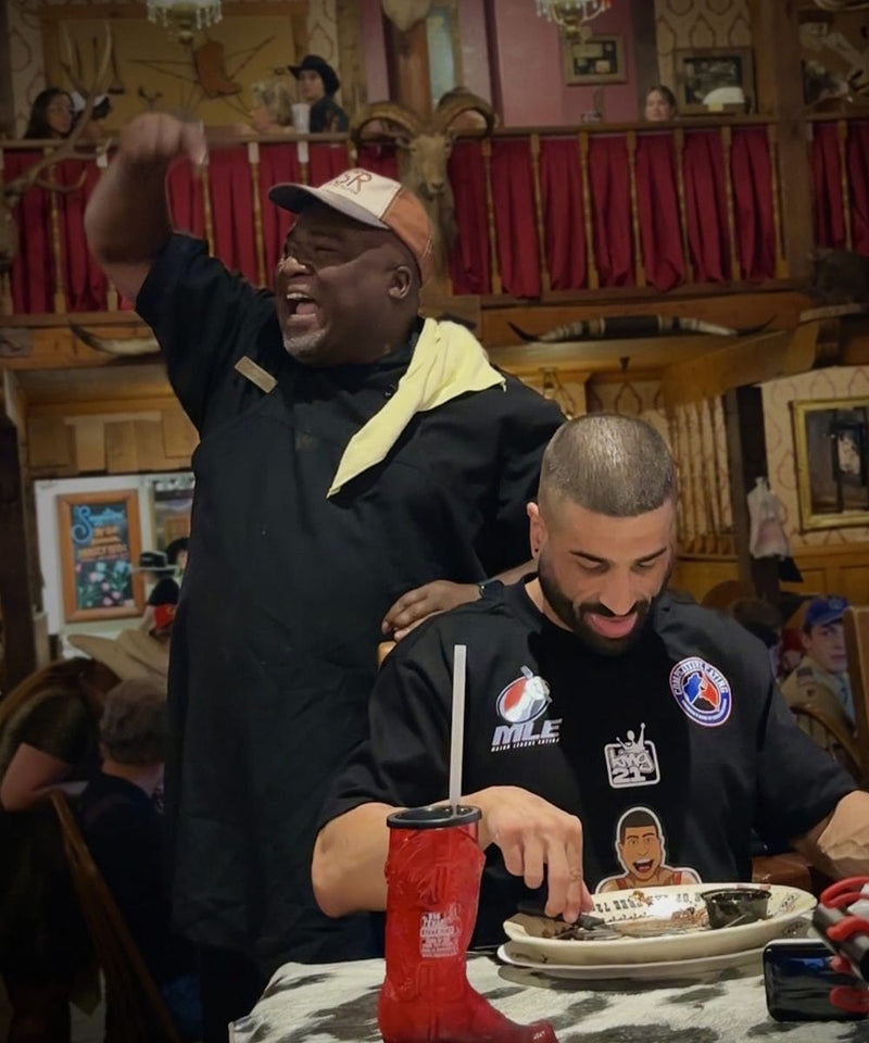 Two men in the big texan dining room with a festive atmosphere, one man yelling to the crowd as the other one is eating off a plate