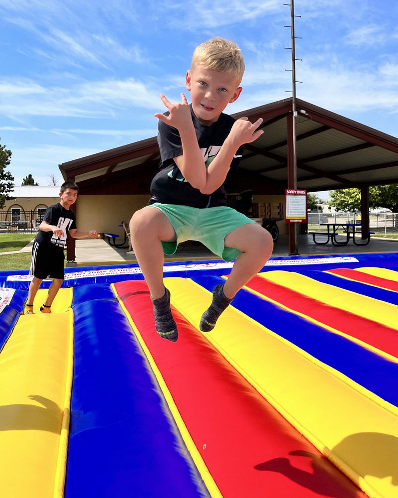 Child jumping on a colorful inflatable jump pad with a clear blue sky in the background