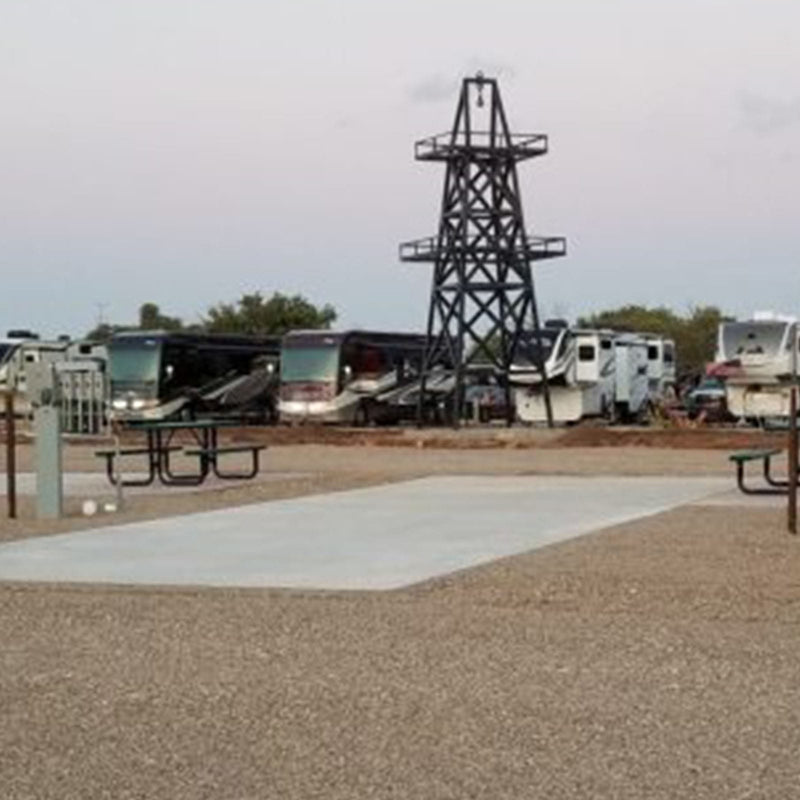 RV park site with concrete pad with multiple RVs and a tall metal structure in the background.