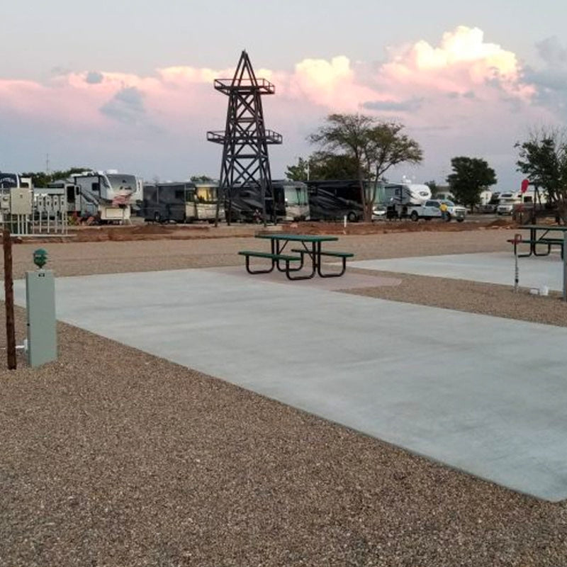 RV park site with concrete pad with picnic tables and a large metal structure under a cloudy sky.