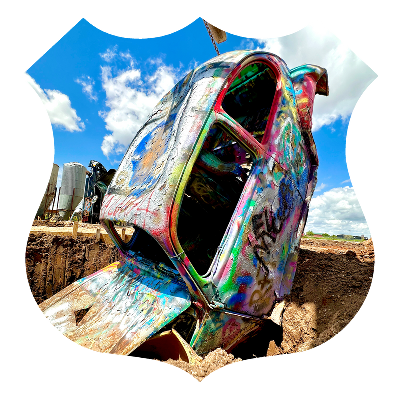 Colorful rusted car sculpture against a blue sky with clouds