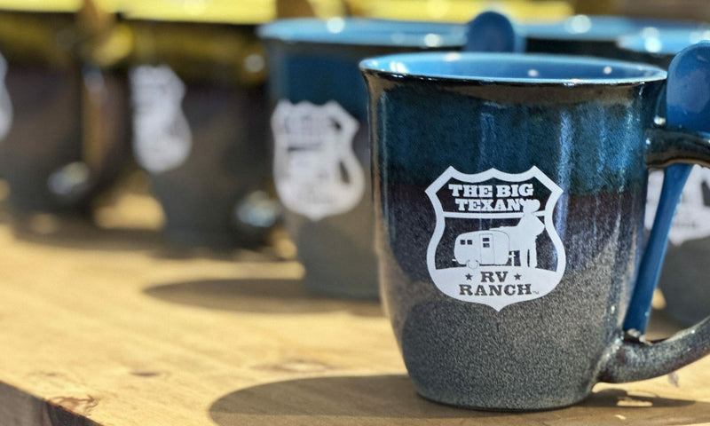 Blue mug with 'The Big Texan RV Ranch' logo on a wooden surface.
