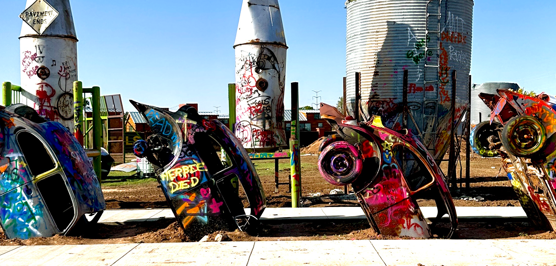 Colorful metal slug bugs buried in the ground with silos in the background
