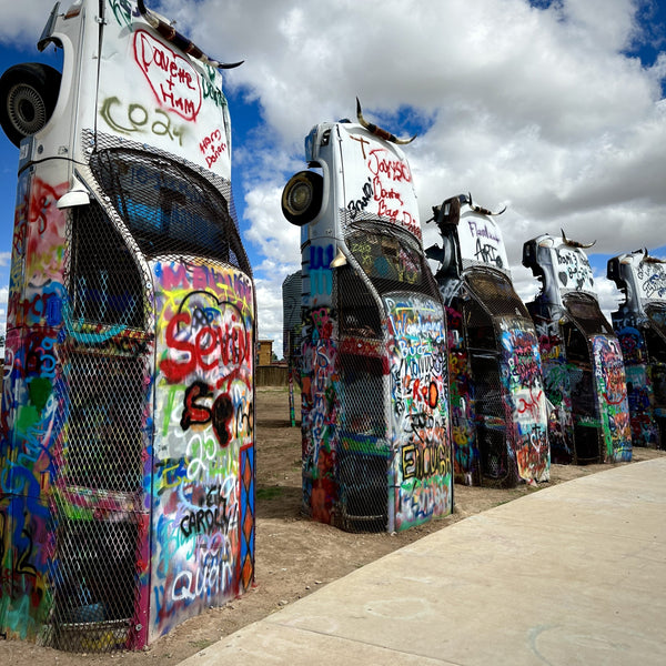 Colorful graffiti-covered cars arranged in a row against a blue sky with clouds.