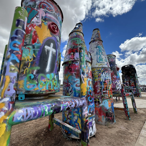 Colorful graffiti-covered metal sculptures against a blue sky with clouds