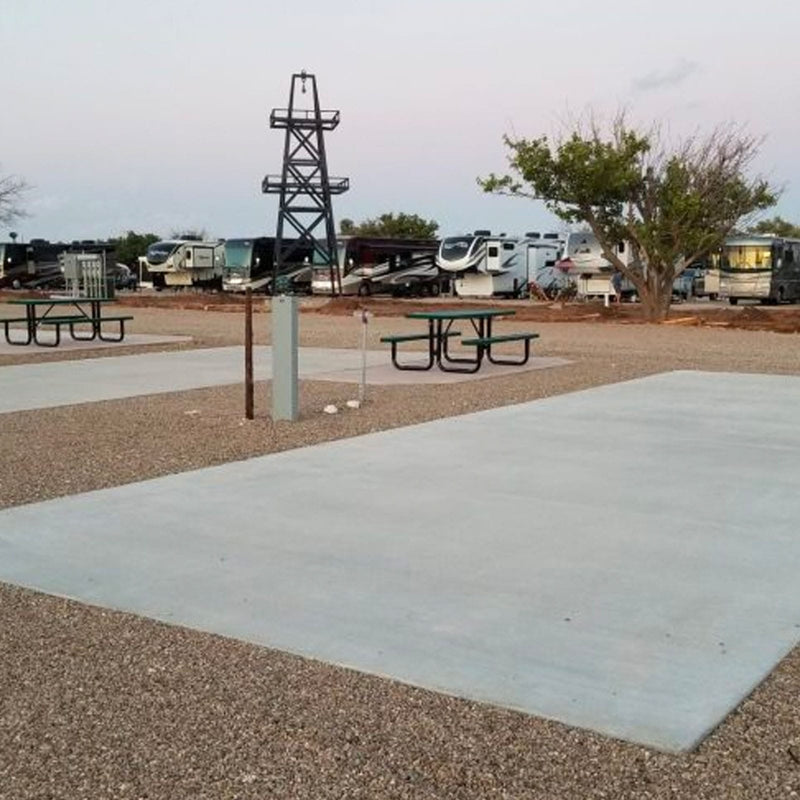 RV park concrete pad site with picnic tables and RVs in the background