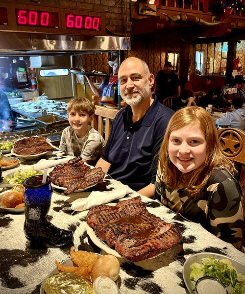 Family of three enjoying a meal with large steaks at a restaurant.