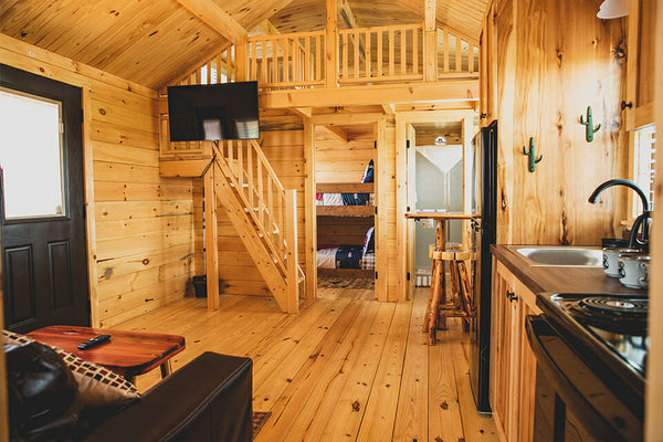 Wooden cabin interior with kitchenette, staircase, and bunk beds.