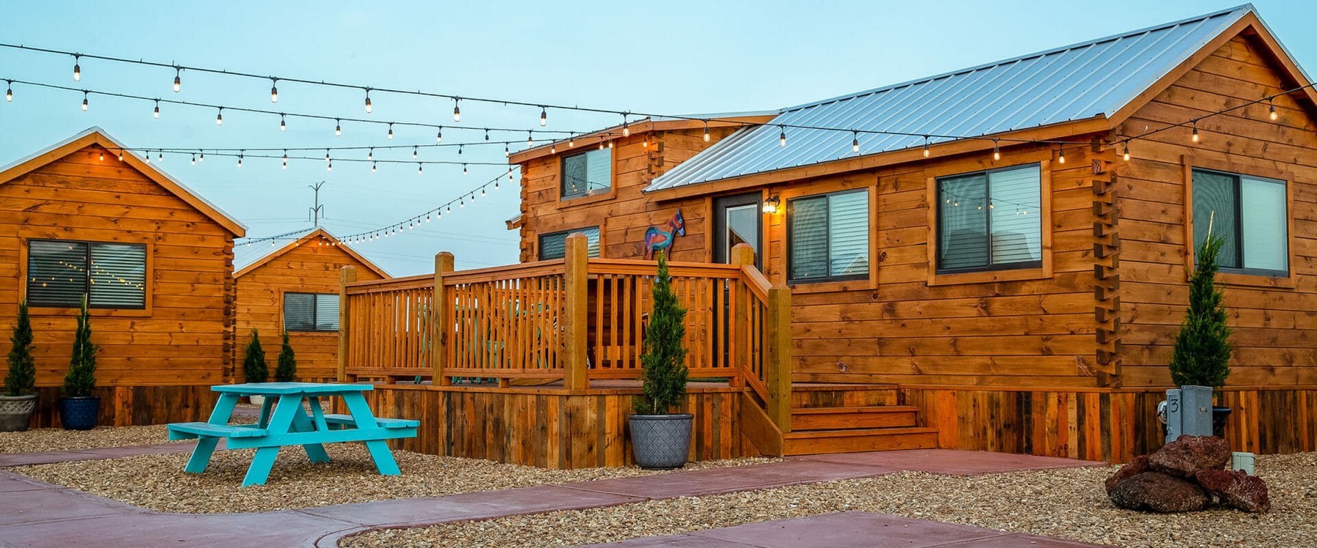 Wooden cabins with a picnic table and string lights in a rustic setting