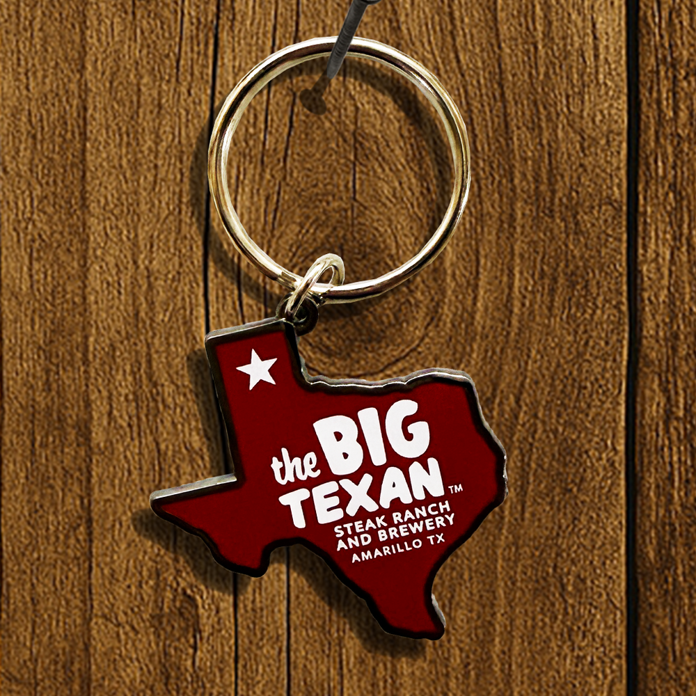 Keychain shaped like the state of Texas with 'the Big Texan' branding on a wooden surface