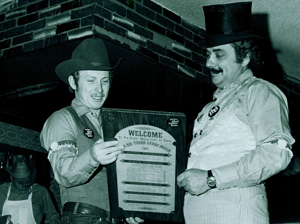 Two men in formal attire holding a menu with a sign in a black and white photograph