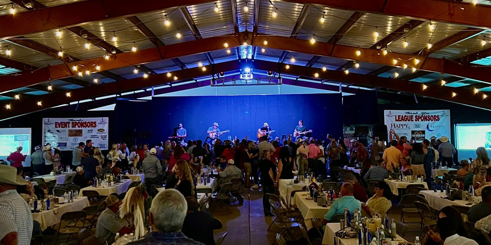Event with people seated at tables, a stage with performers, and event sponsors displayed on screens.