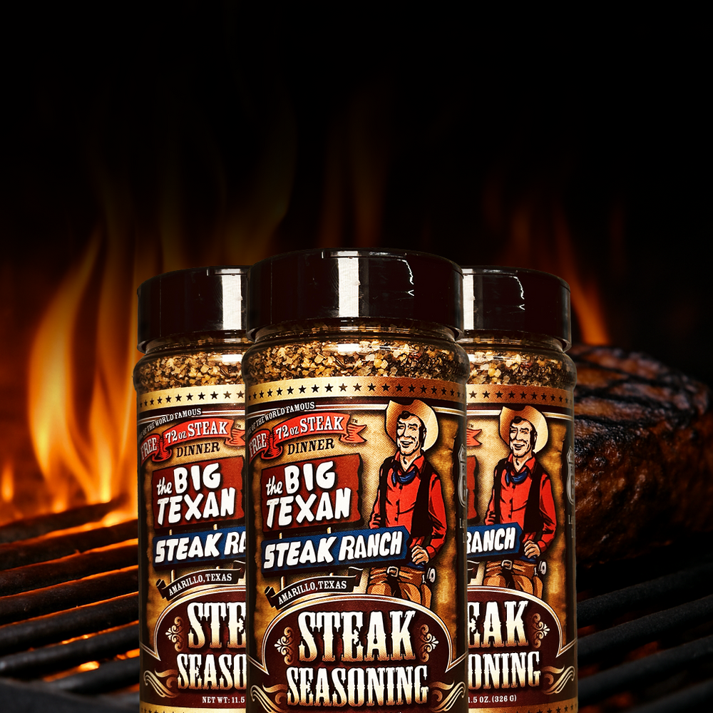 Three jars of Big Texan Steak Ranch seasoning with a grill and flames in the background