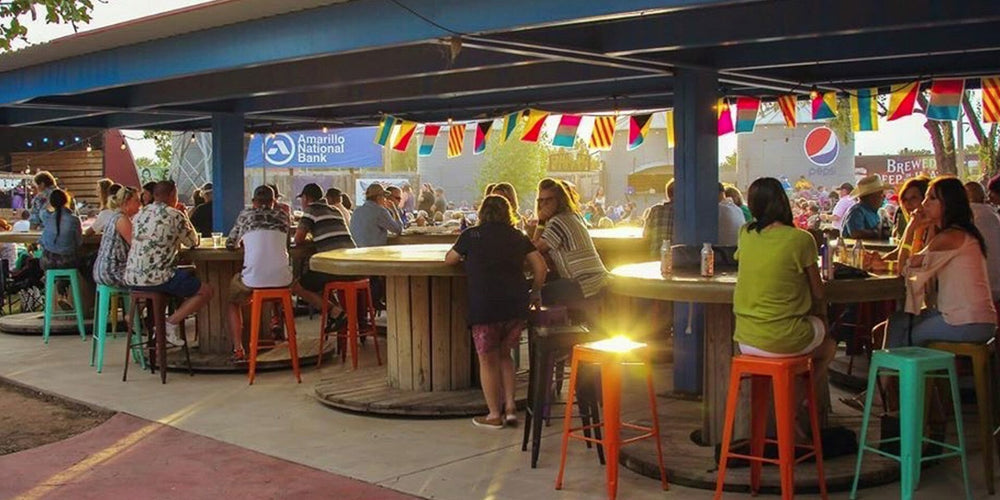 People sitting at outdoor tables under a canopy with colorful flags and signs.